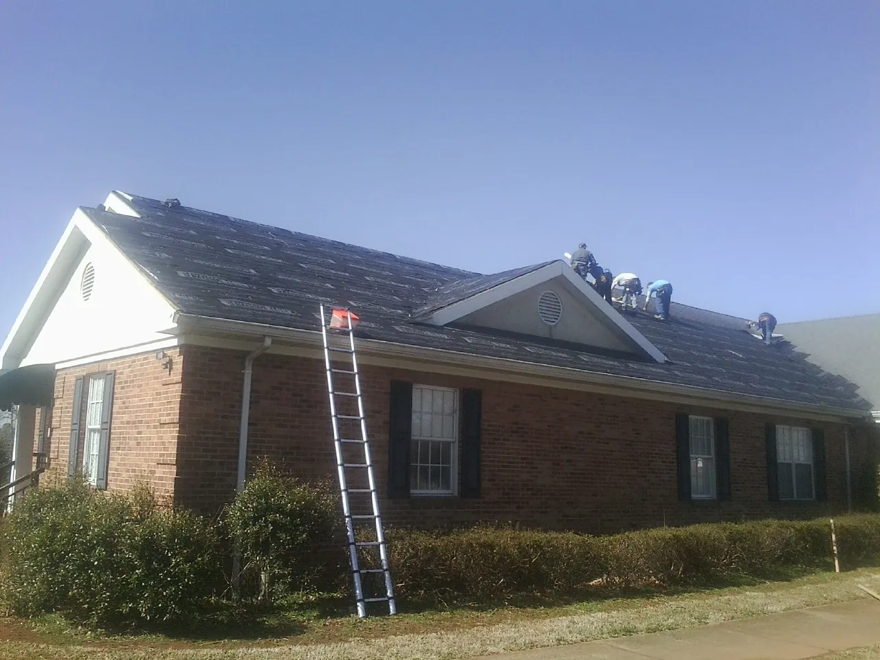 Crew tearing shingles off a brick ranch roof with a ladder set — Emergency Roof Repair work by our crew in Saint Meinrad