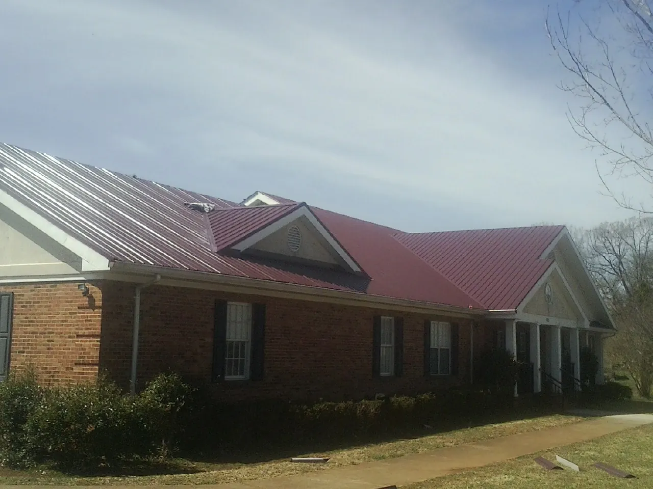 Red metal roof with gabled entries on a long brick building, from a Hail Damage Roof Repair job in Saint Meinrad