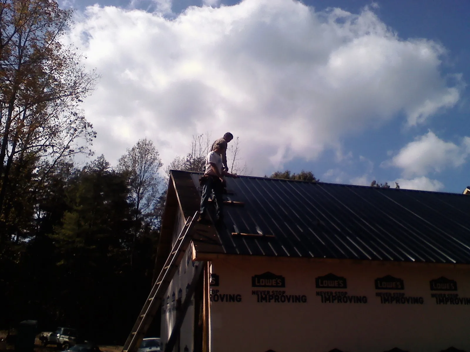 Roofer fastening dark metal panels high against a cloudy sky, from a Roof Inspection job in Saint Meinrad
