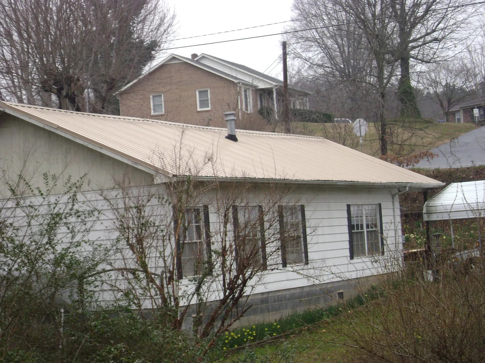 Tan metal roof on a white sided house set into a hillside in Saint Meinrad
