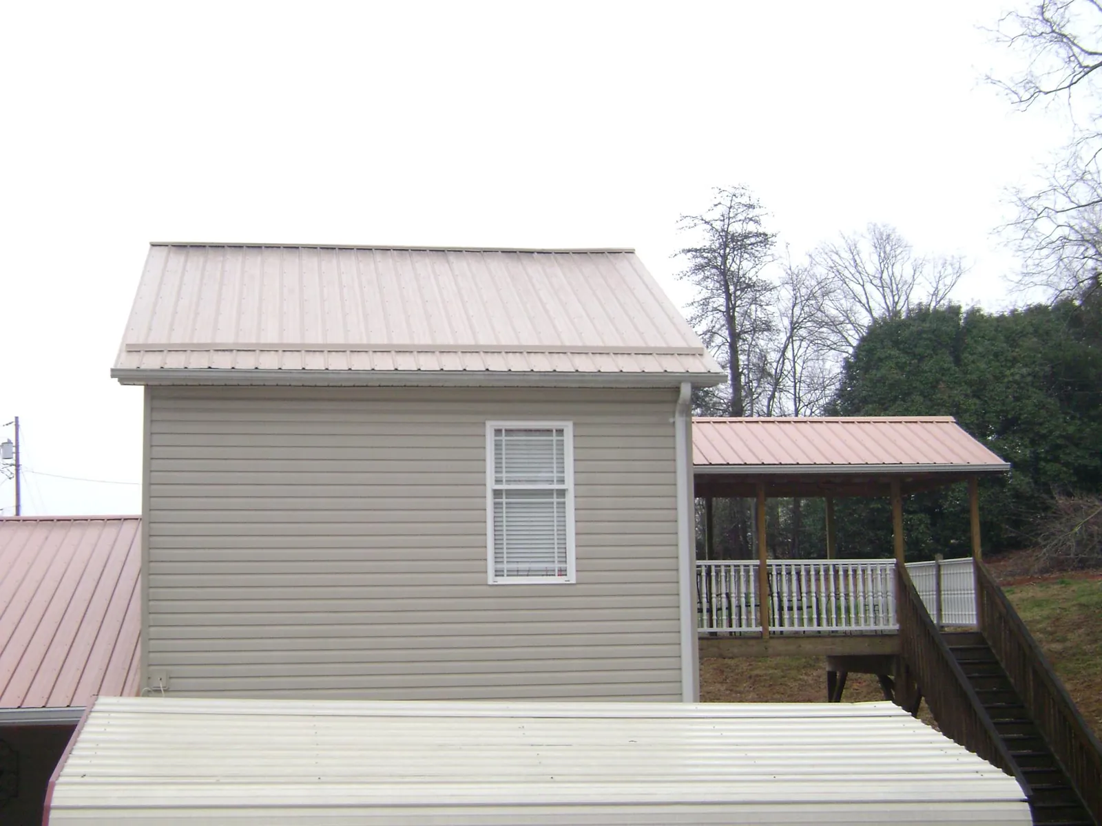 Tan metal roofs on a two story addition and attached porch, from a Roof Replacement job in Saint Meinrad
